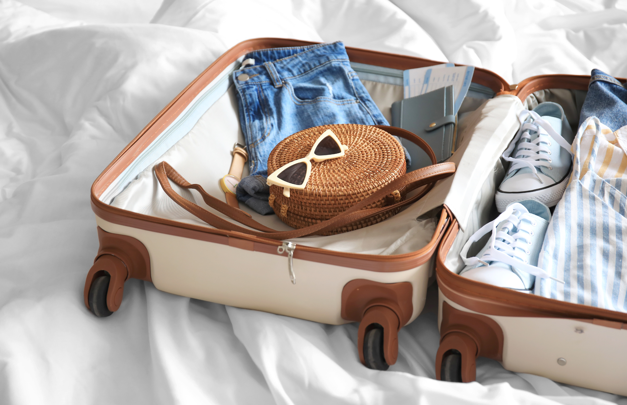 Suitcase on a bed with a jacket, purse, sunglasses, and other items