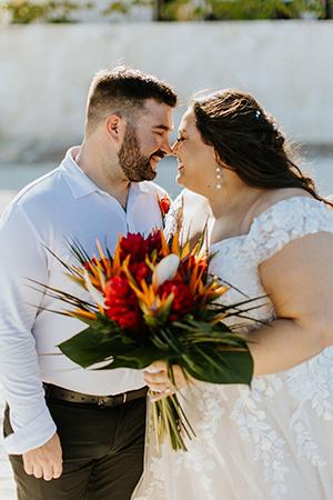 Happy couple touch noses while bride holds a tropical bouquet at a destination wedding in Mexico