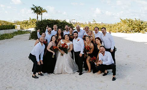 wedding party group shot in the sand with greenery in the background