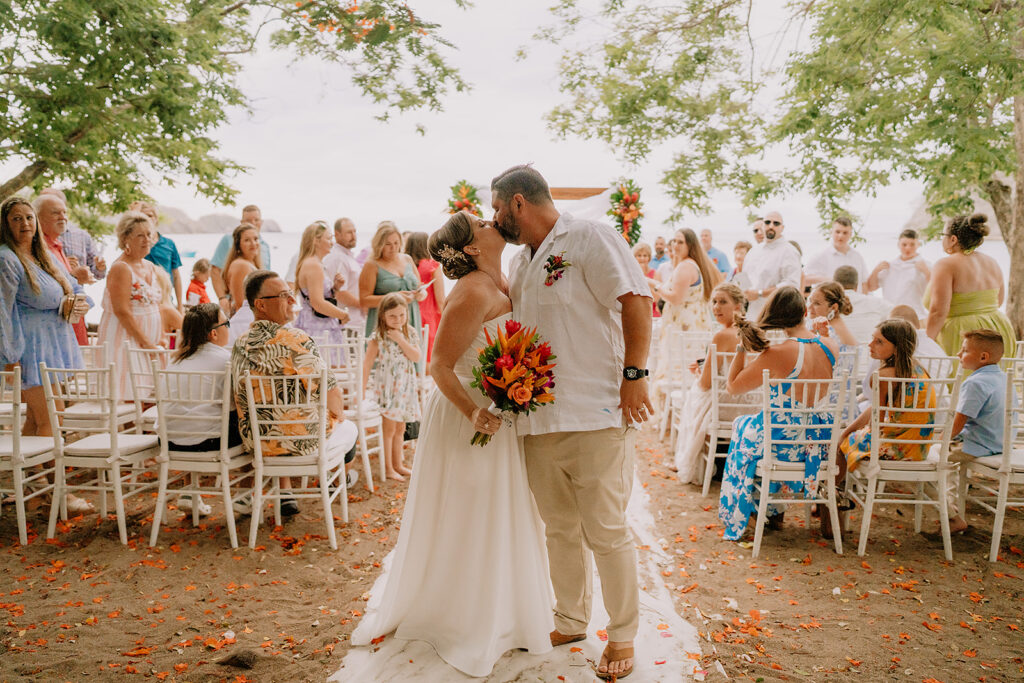 bride and groom newly married kissing at the end of the aisle-budgeting for a destination wedding