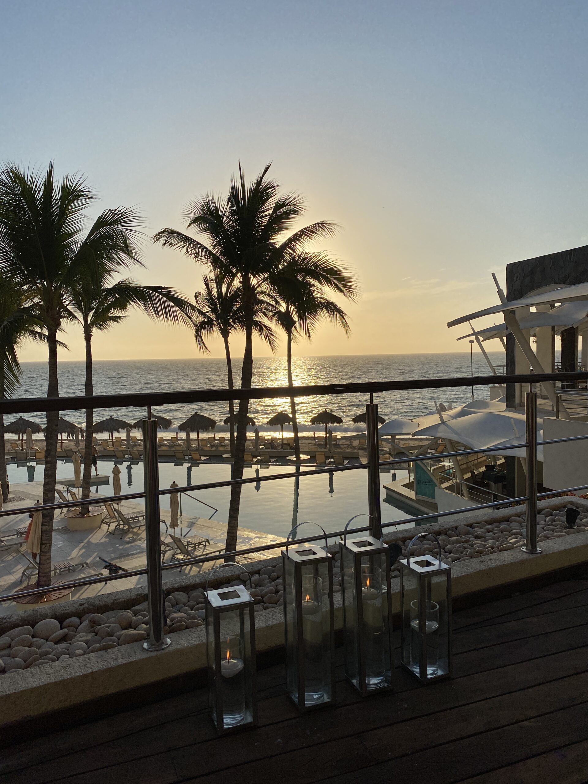 Sunset view with palm trees from a patio overlooking the ocean at an LGBTQ+ friendly resort, perfect for romantic moments.