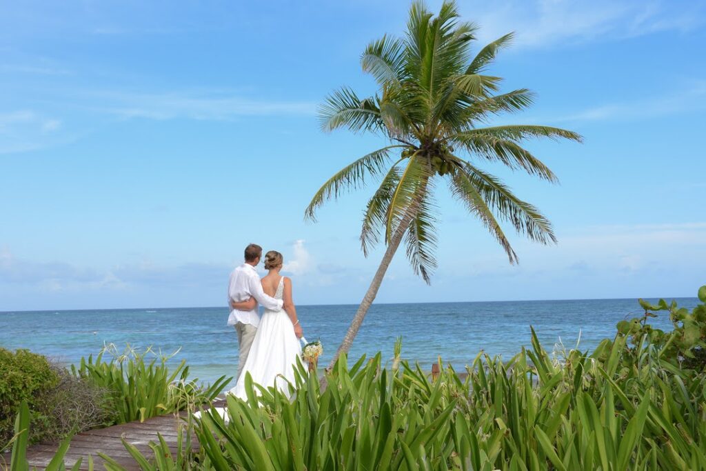 Bride and groom standing on a tropical beach, embracing after their ceremony planned by a wedding coordinator at a destination resort.