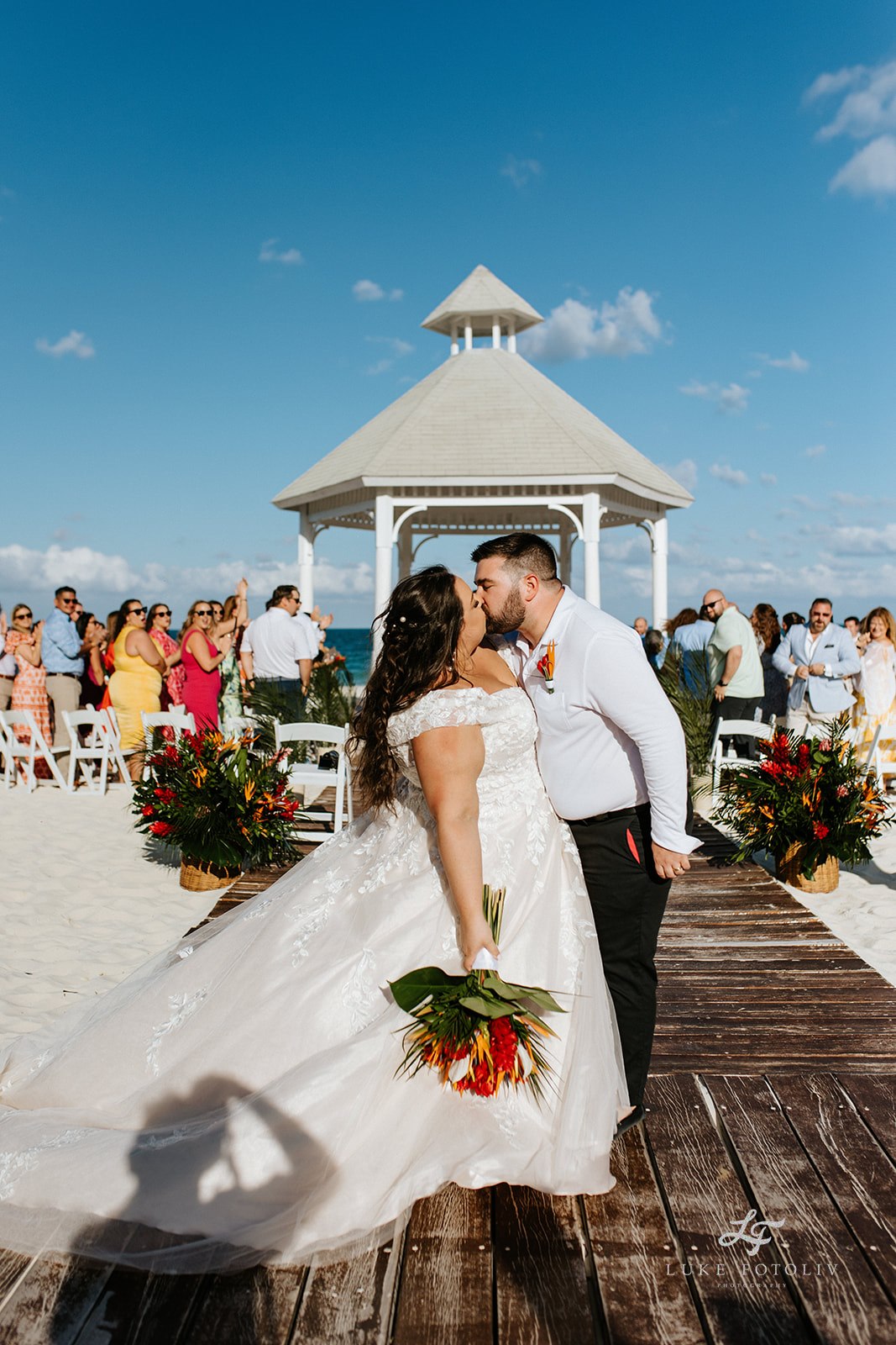 Newlyweds kiss in front of their beach ceremony setup, seamlessly organized by a wedding coordinator and resort team.