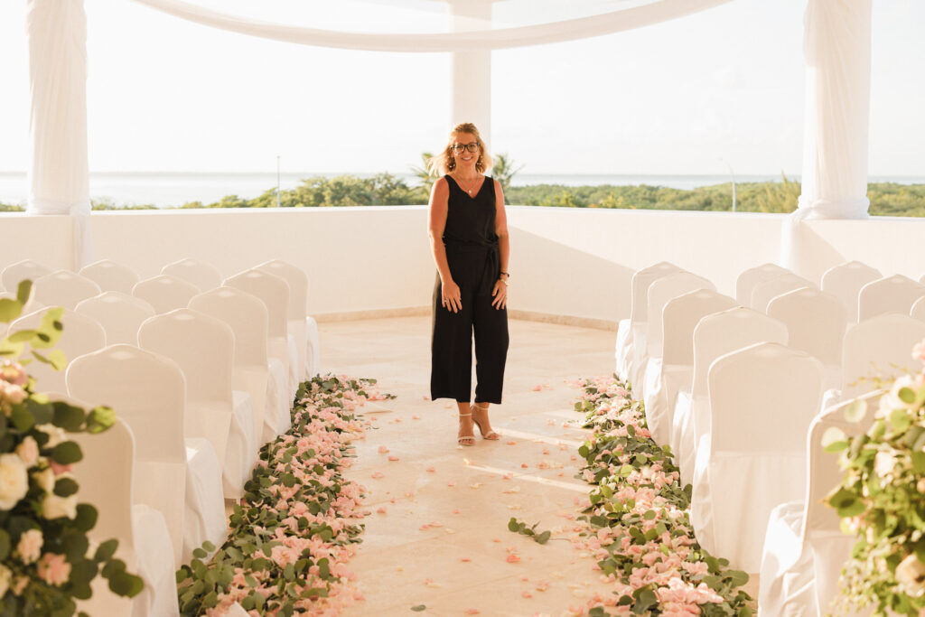 Wedding coordinator standing in a floral aisle at a rooftop destination wedding, ready to greet guests and oversee the event.