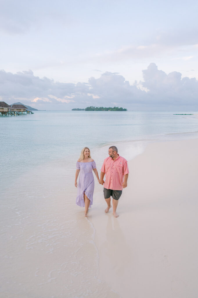 Couple walking hand in hand along the turquoise waters in Bora Bora, one of the most iconic luxury honeymoon destinations.