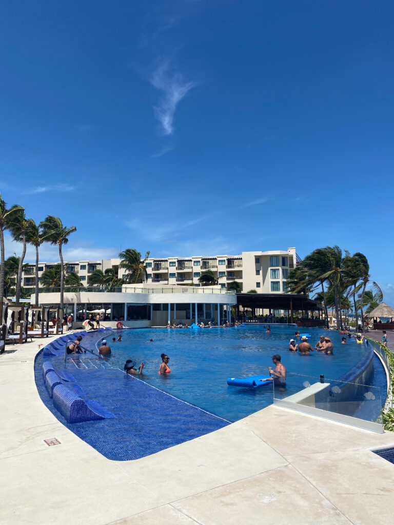 Guests relaxing in a large infinity-edge pool with submerged loungers at a modern tropical resort.