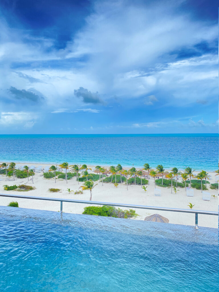 Infinity pool overlooking white sand beach and palm-lined shoreline with vibrant turquoise ocean views.