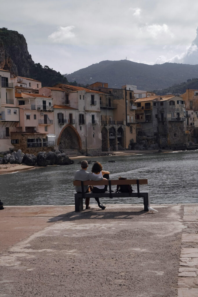 Couple sitting by the water in a historic Italian town, enjoying a romantic honeymoon itinerary moment.