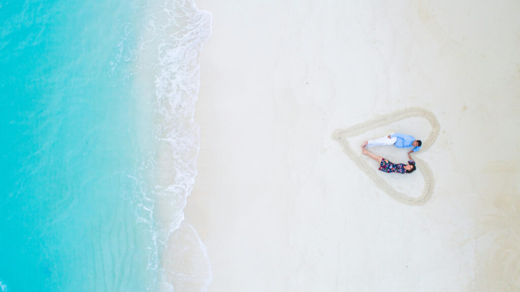 Couple lying in a heart shape on the sand during a beach honeymoon itinerary photo shoot.