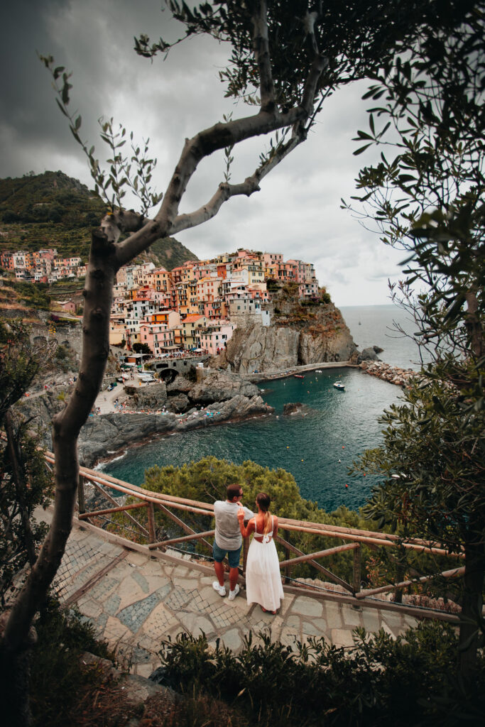 Couple overlooking colorful coastal village in Italy, enjoying a scenic moment on their honeymoon itinerary.