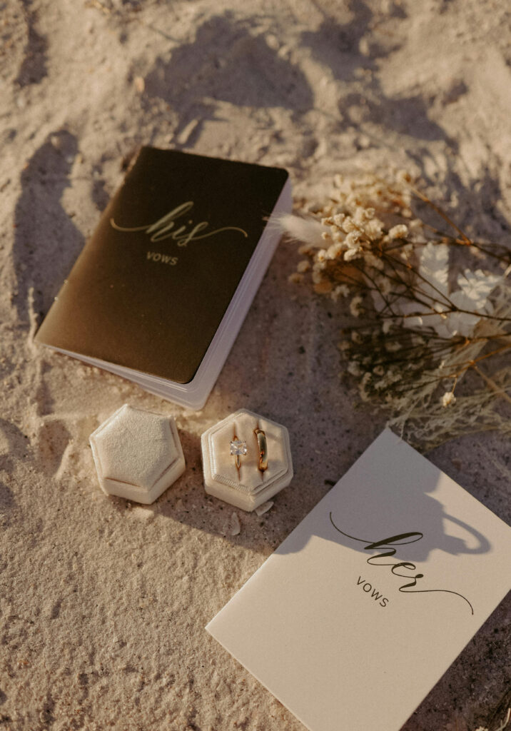 Wedding rings and vow books styled on sand.