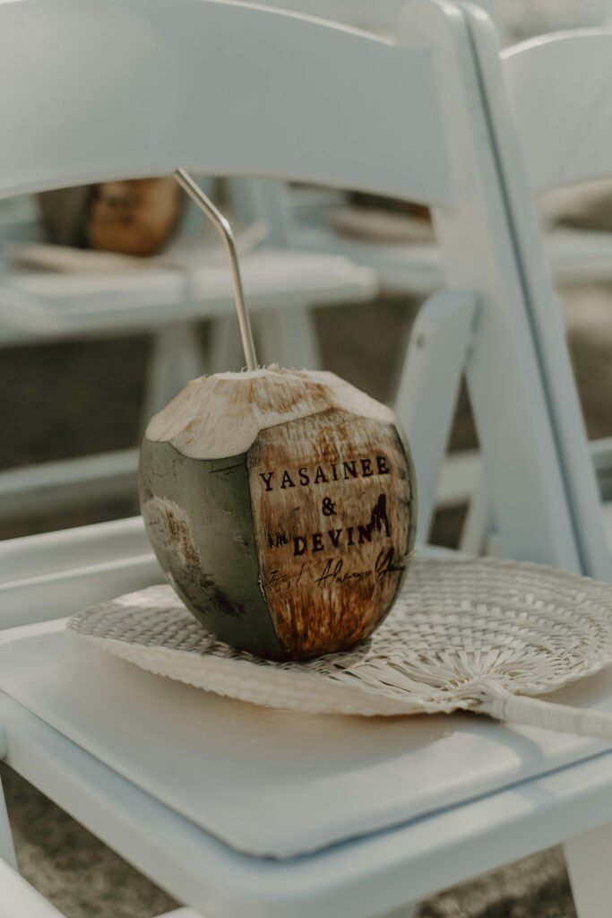 Personalized coconut drink and woven fan as eco friendly wedding ideas for tropical guest seating.