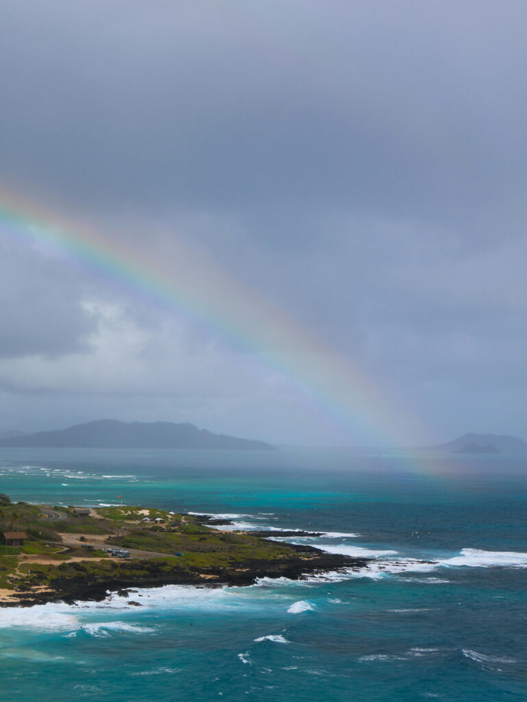 Rainbow over turquoise ocean under cloudy skies—perfect setting for a romantic wedding in rainy season.
