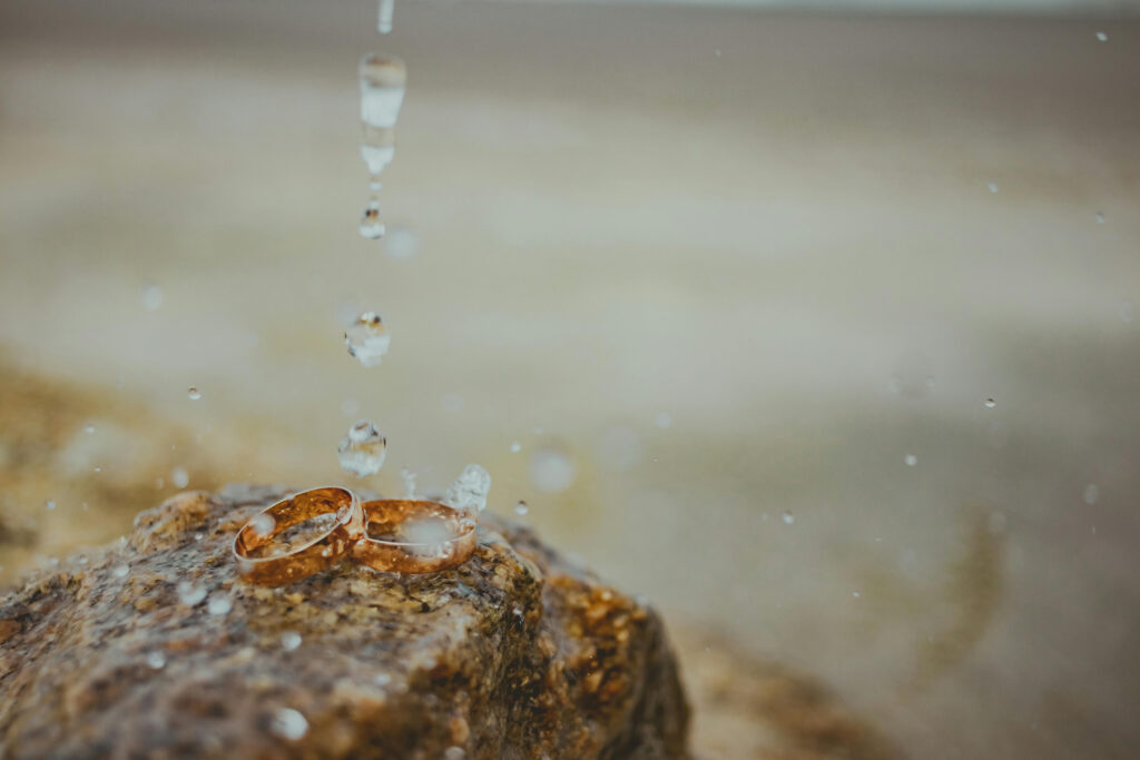 Two gold wedding rings on wet stone with raindrops