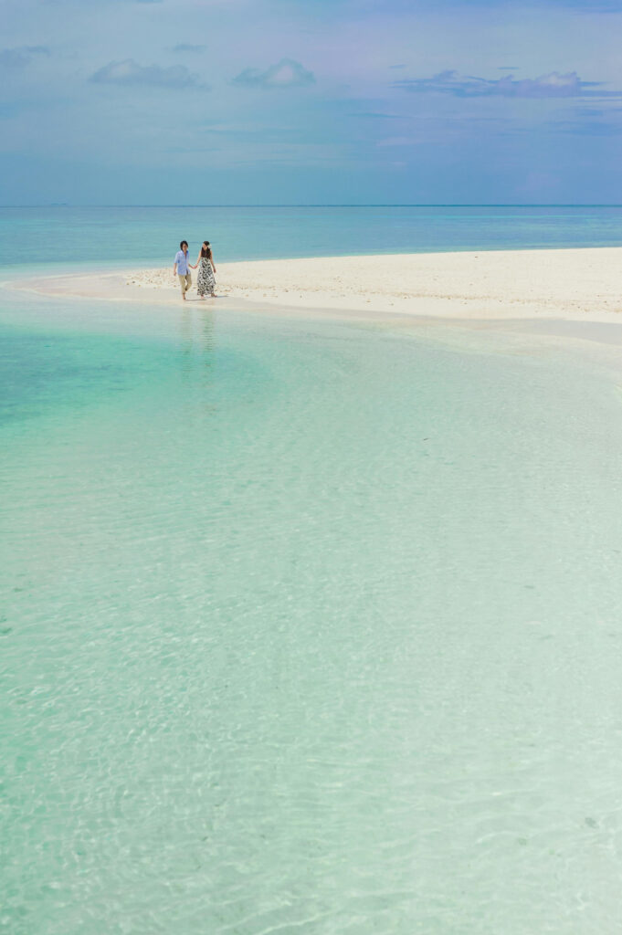 Couple walking hand-in-hand on a quiet beach during a tropical wedding retreat by turquoise water.