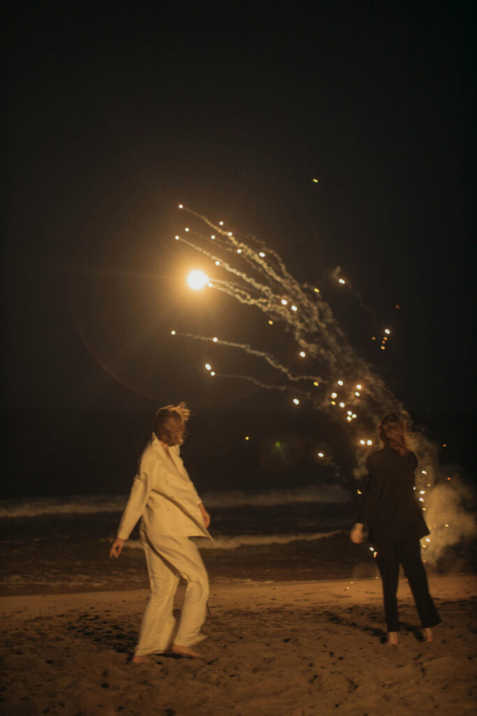 Two people enjoying fireworks on the beach at night, capturing a magical and celebratory wedding moment.