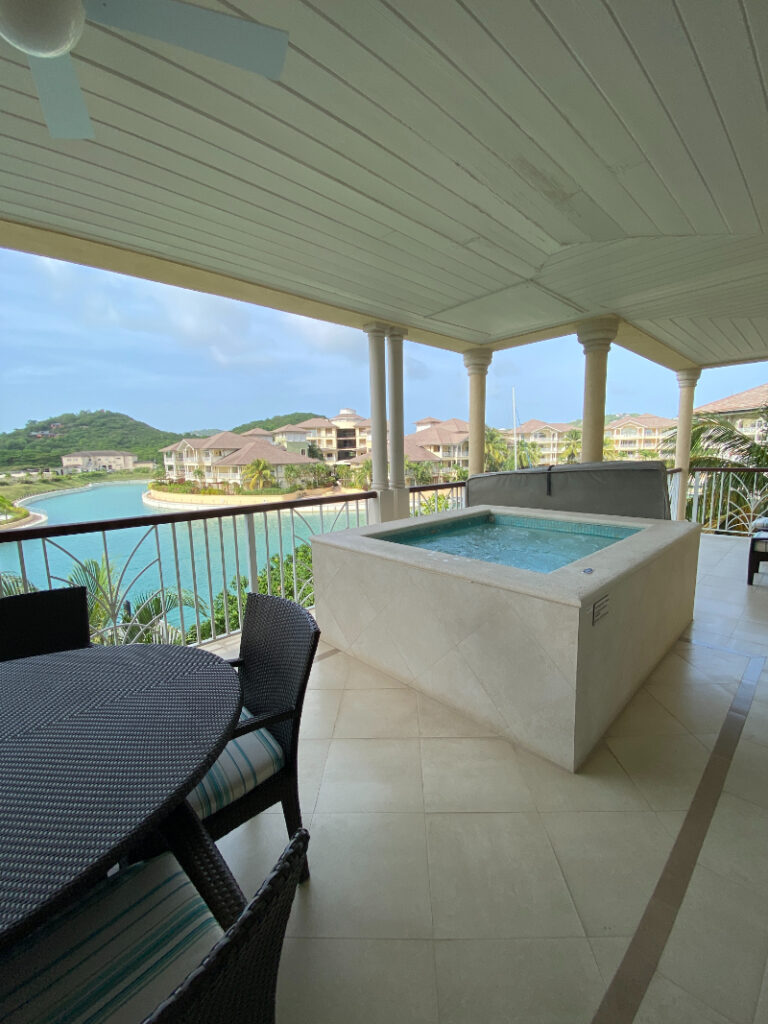 Private terrace with a hot tub and dining set overlooking a calm lagoon and luxury resort villas.