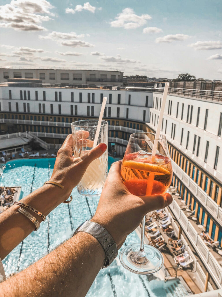 Couple cheers with cocktails above resort pool during a mid-week destination wedding celebration abroad.