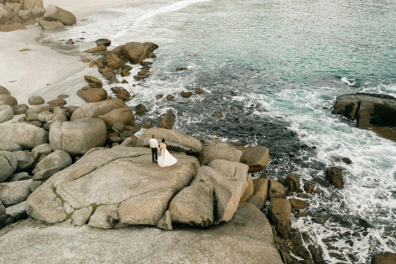 Couple stands on oceanfront rocks in Mexico, capturing a bold moment from their wedding guest experience guide.
