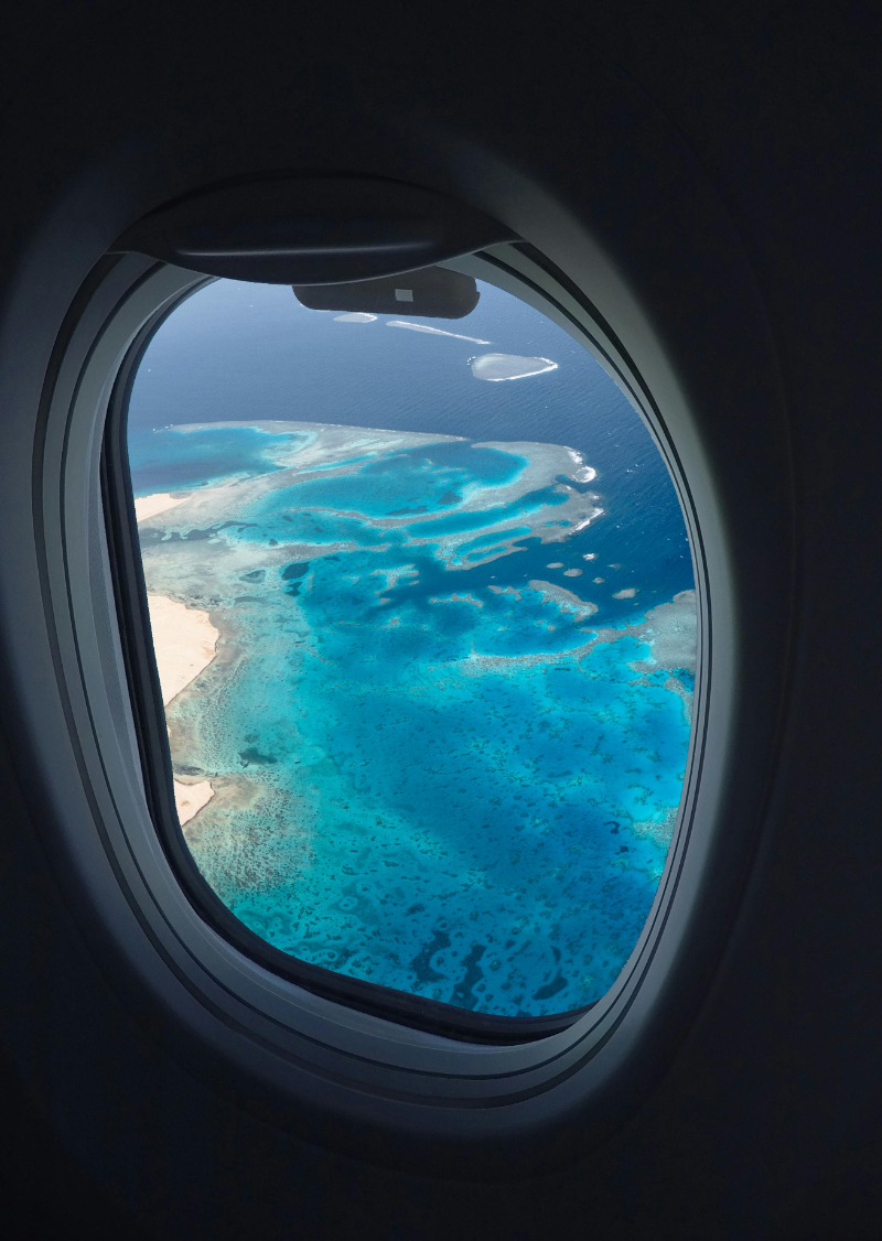 View from airplane window of bright turquoise ocean and reef, reminding travelers to avoid honeymoon travel mistakes.