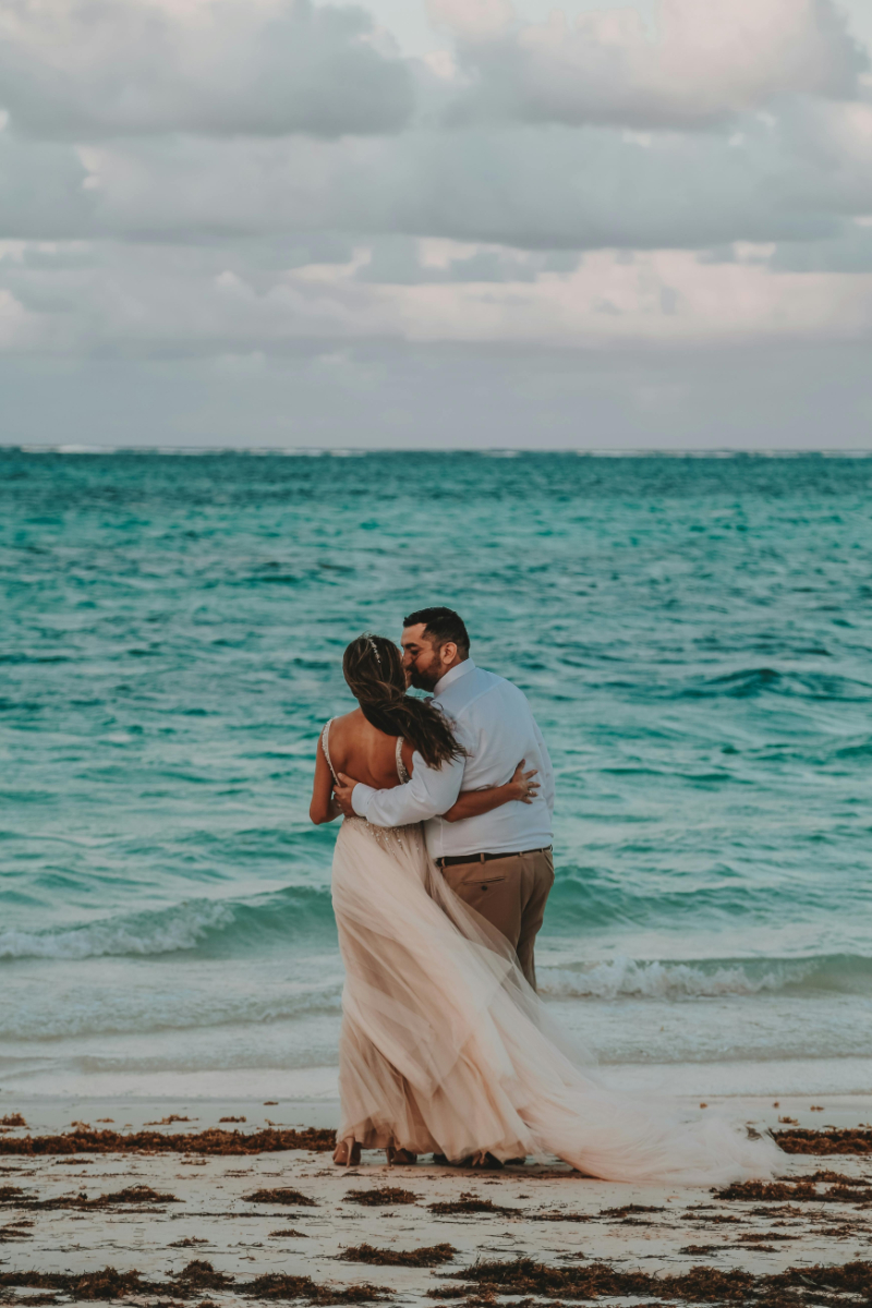 Bride and groom share a quiet moment by the ocean, her dress flowing in the seaside breeze.