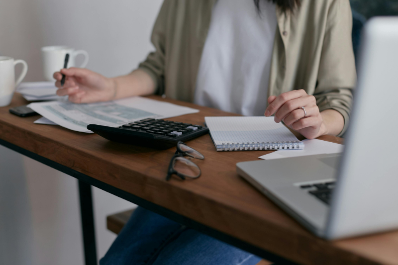 Person working at a desk with a calculator, notebook, and laptop, budgeting and reviewing financial plans.