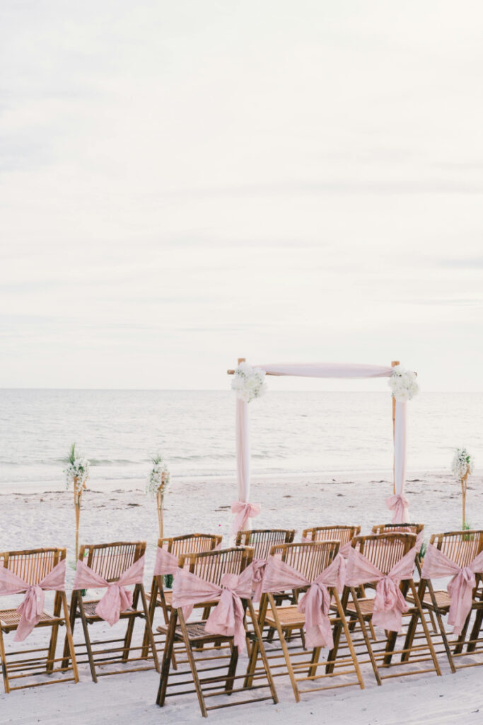 Beach ceremony setup with pink ribbons and ocean backdrop, perfect for a luxe destination wedding.