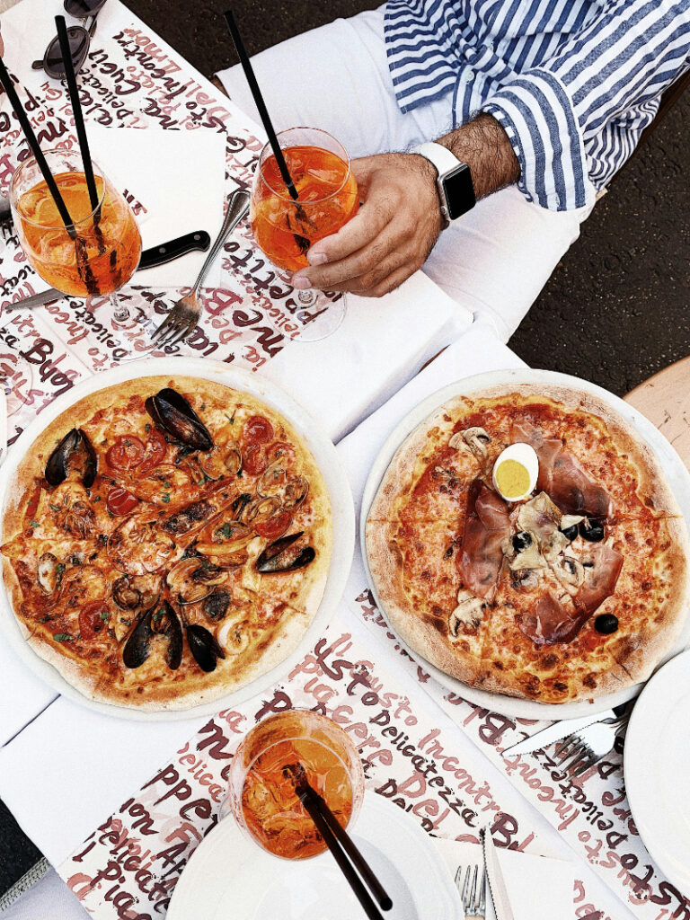 Two gourmet pizzas with Aperol spritzes on a cafe table, perfect for a romantic European meal.