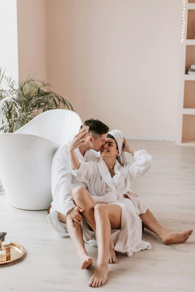 Couple in bathrobes laughing and cuddling on the floor, capturing a cozy moment of where to honeymoon.