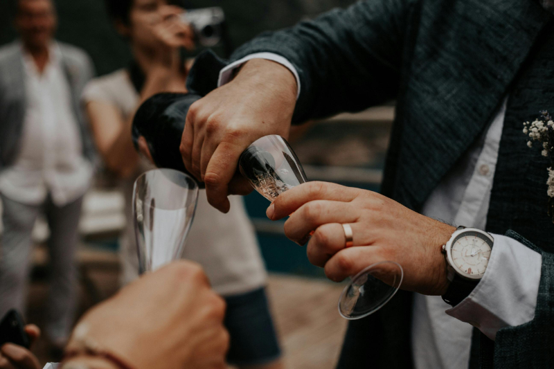 Close-up of champagne being poured into glasses during an outdoor wedding celebration with guests nearby.