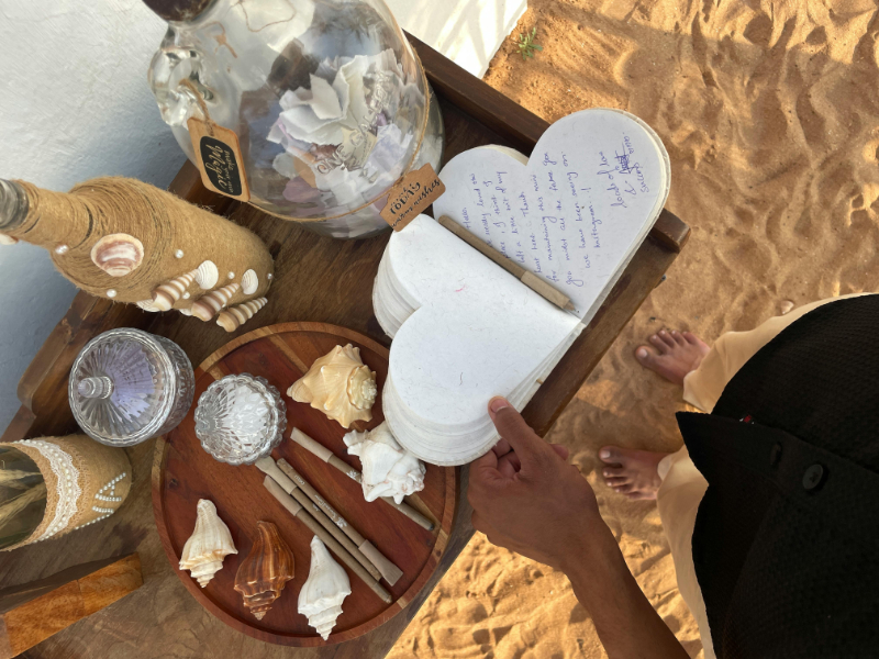 Beach-themed guestbook table for attending a destination wedding, featuring seashell decor, handwritten notes in a heart-shaped book, and a barefoot guest.