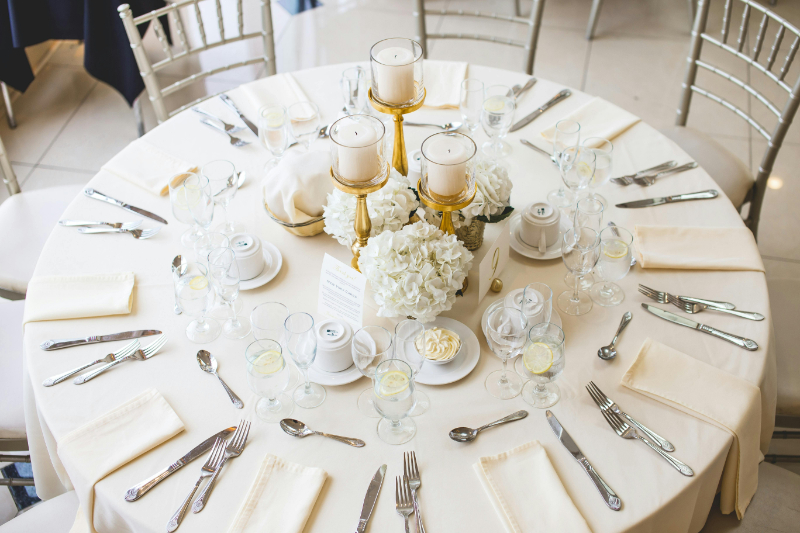 Elegant wedding reception table set with white florals, candles, and formal place settings for eight guests.