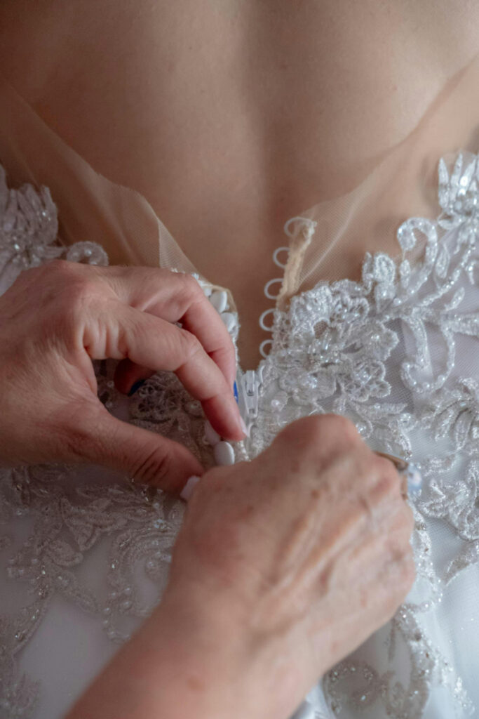 Hands buttoning bride’s lace gown, a quiet moment behind the scenes of a destination wedding.