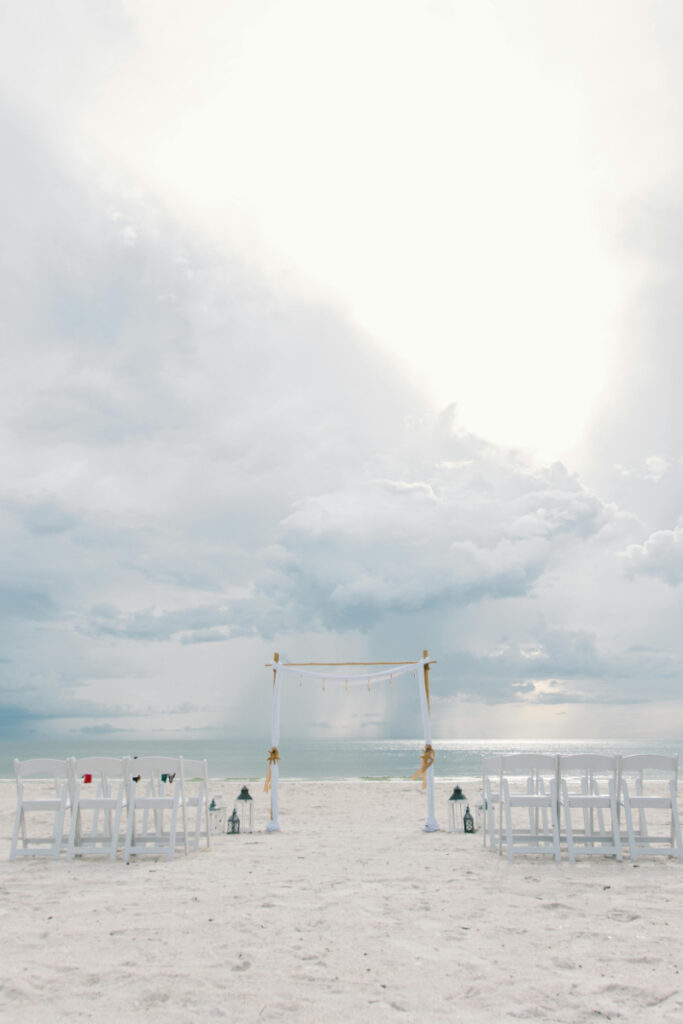 Beach ceremony setup under cloudy skies, showing weather uncertainty behind the scenes of a destination wedding.
