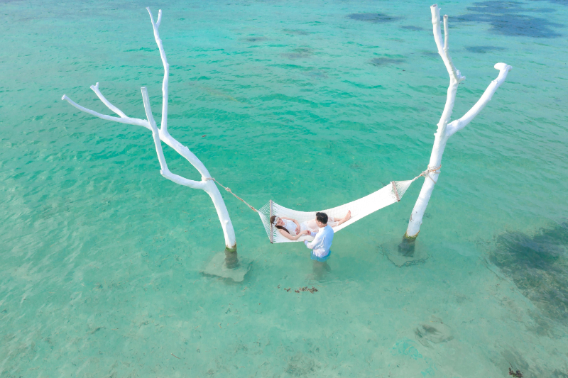 Couple relaxing on a hammock over clear turquoise water, enjoying peaceful island vibes on their honeymoon.