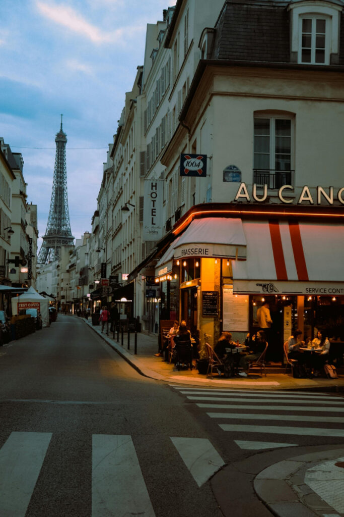 Cozy Parisian street scene at dusk with the Eiffel Tower in the background and a glowing brasserie.