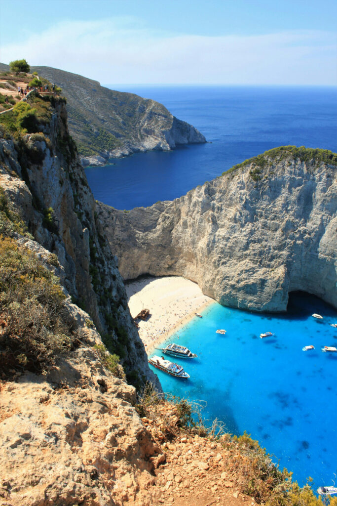 Dramatic coastal cliffs overlooking turquoise water and secluded beach in southern Europe.