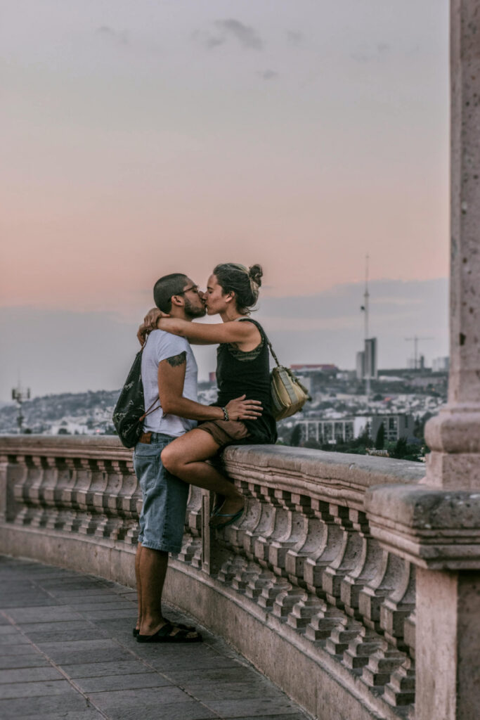 Europe honeymoon couple kissing at sunset overlook with romantic city skyline backdrop.