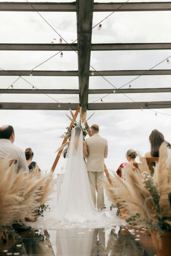 Bride and groom at beachfront destination wedding ceremony under modern wooden arch.