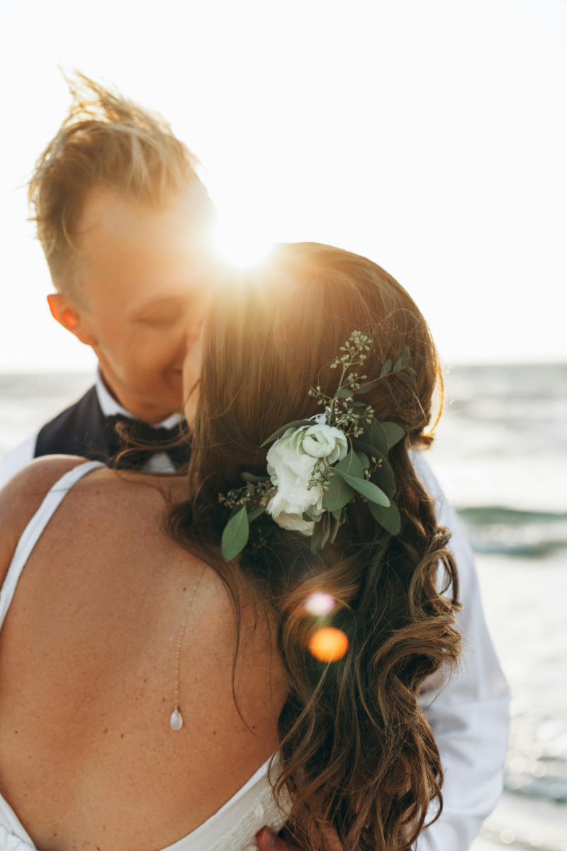 Close up of bride and groom embracing on beach at sunset with floral hair detail.