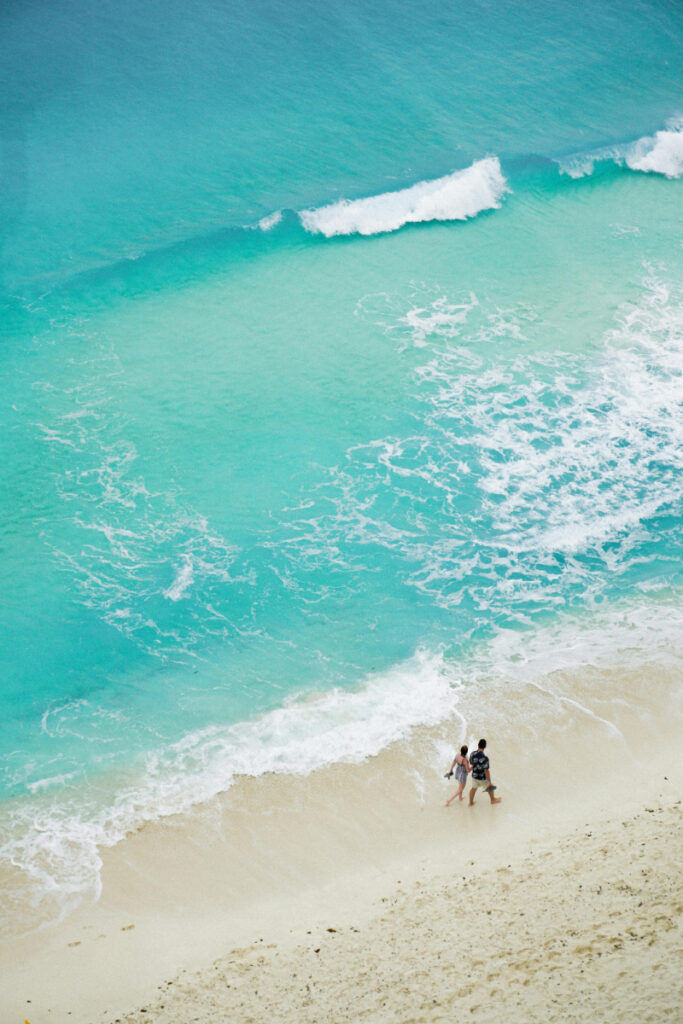 Couple walking along turquoise shoreline during romantic honeymoon in Mexico getaway.