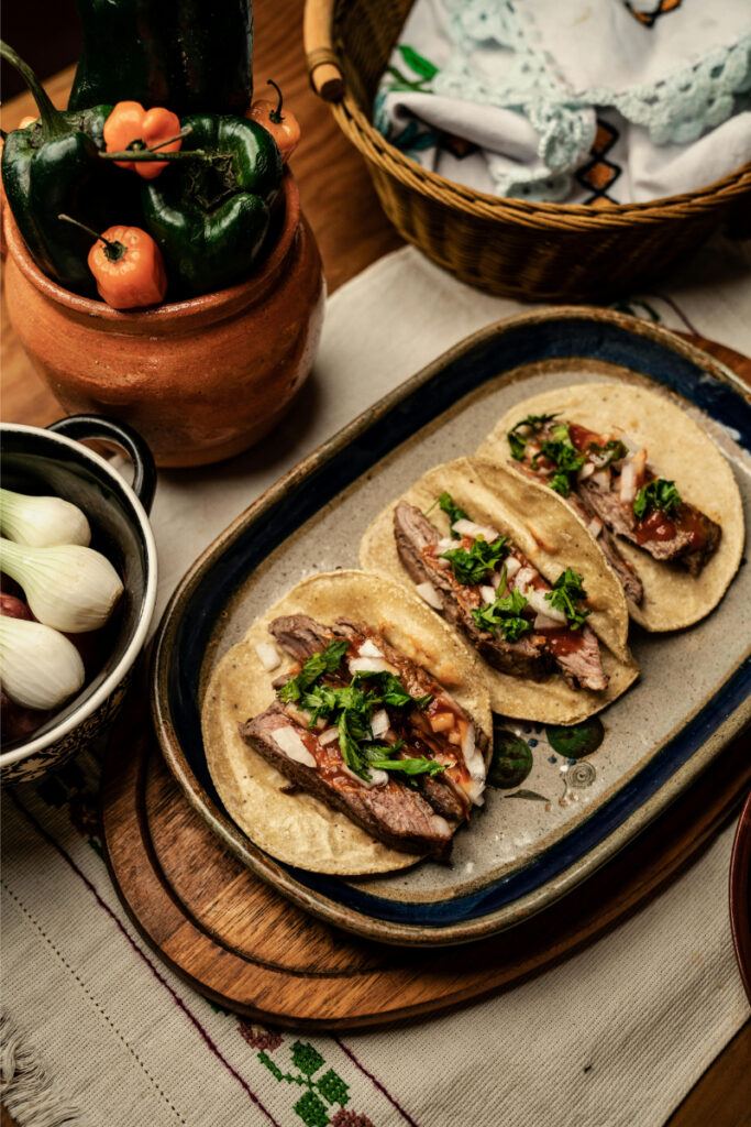 Plate of fresh street tacos with grilled meat, onions, and cilantro on rustic table.