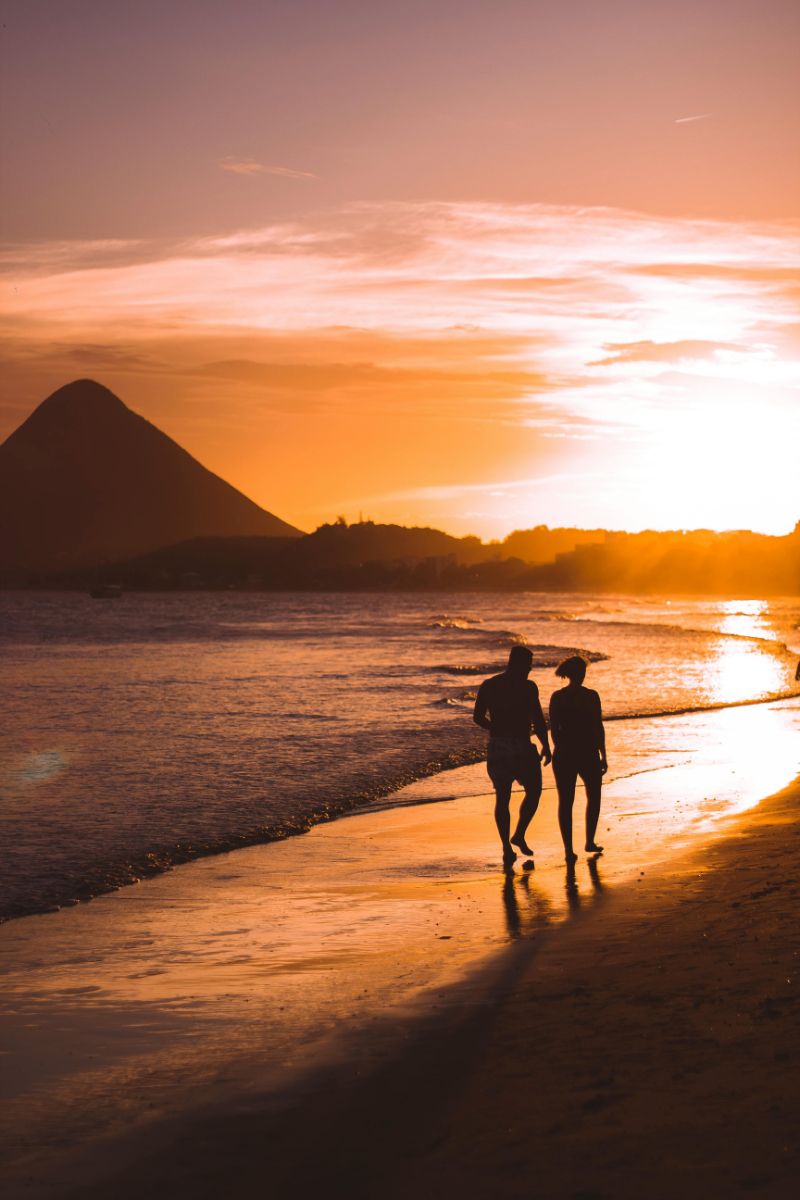 Silhouetted couple walking along beach at sunset with glowing sky and waves.