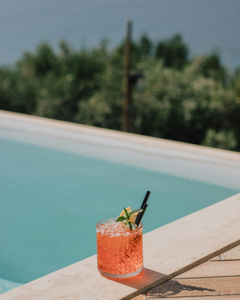 Pink cocktail with mint and lemon garnish beside a serene resort pool.