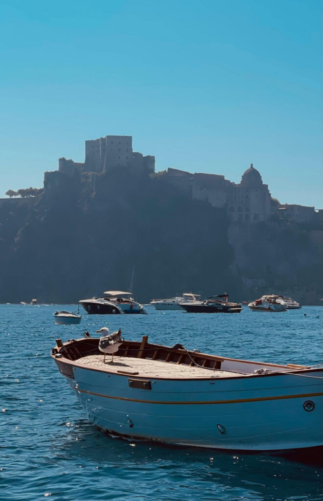 Coastal Italy scene with small boat, clear blue water, and cliffside village in soft sunlight