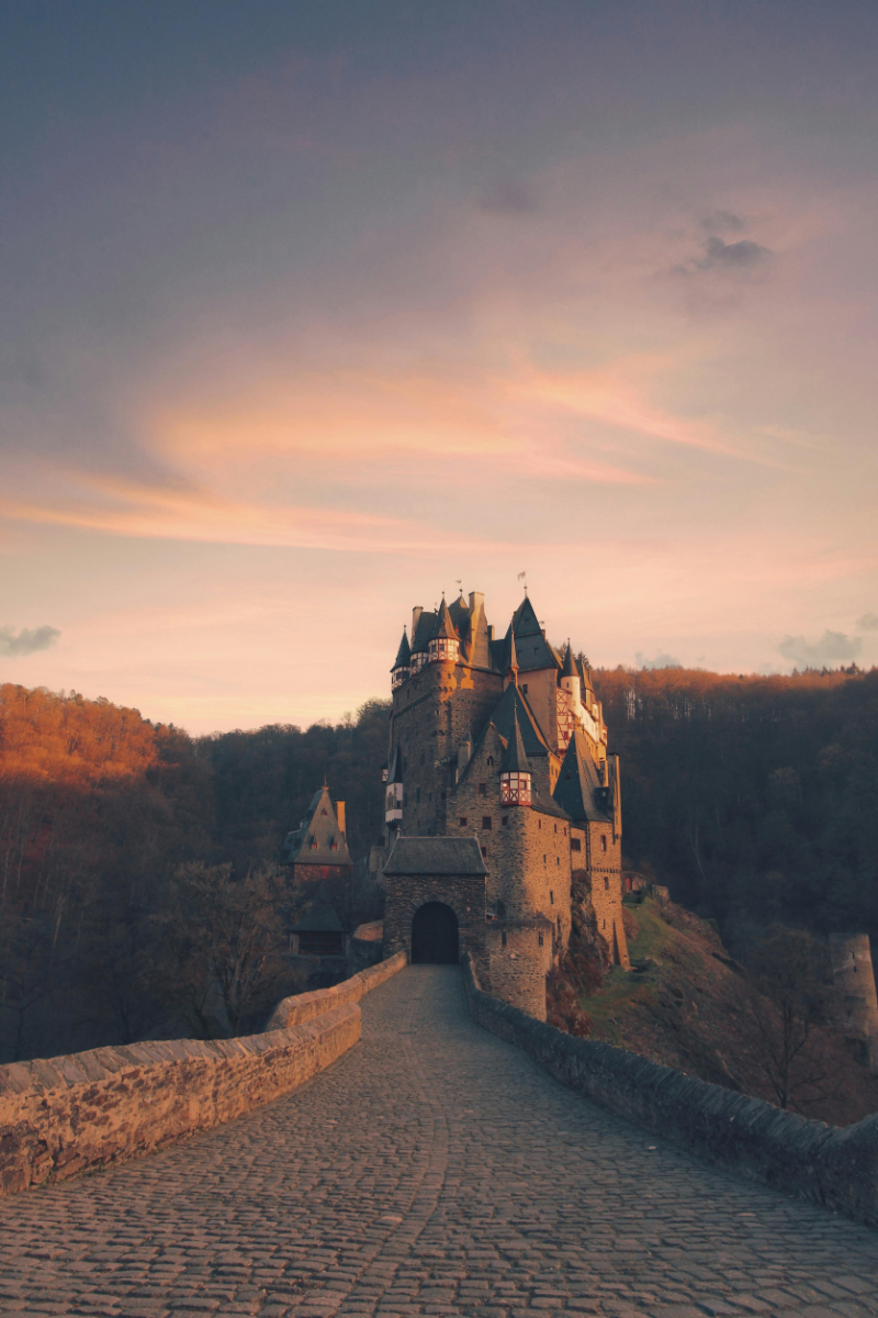Fairytale castle at sunset with soft pink sky, forest backdrop, and warm glowing lights