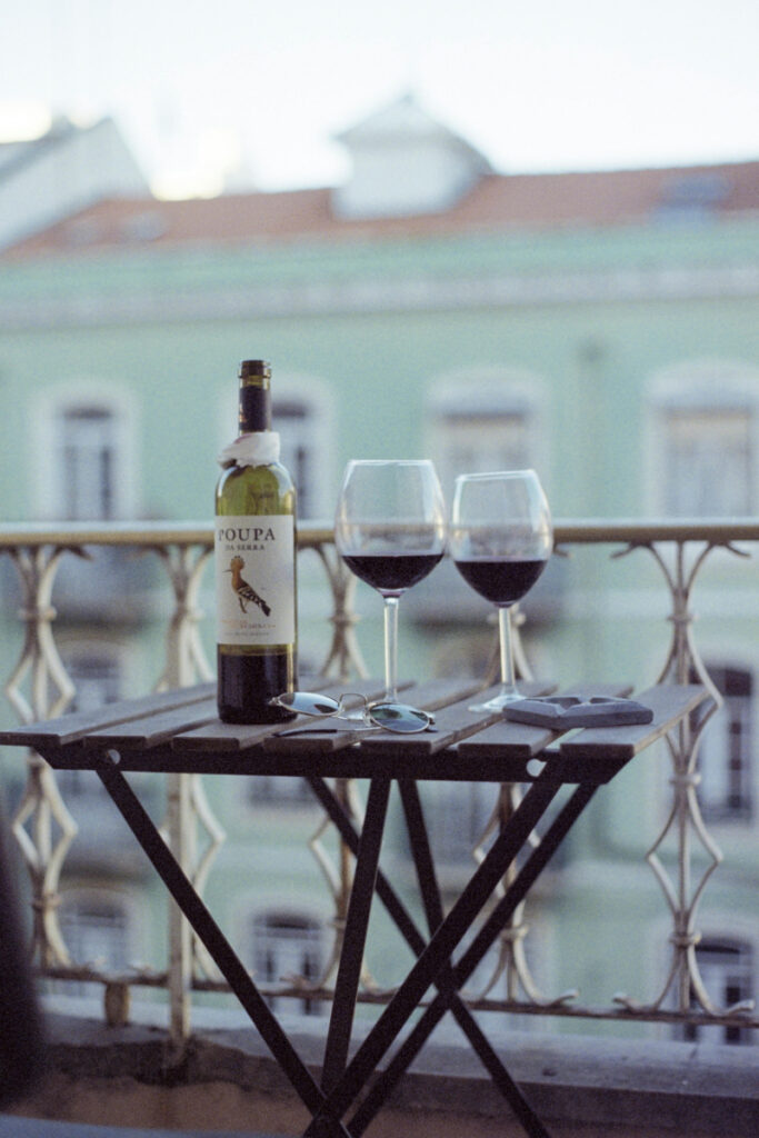 Balcony table with wine glasses, bottle, and soft city view in warm evening light
