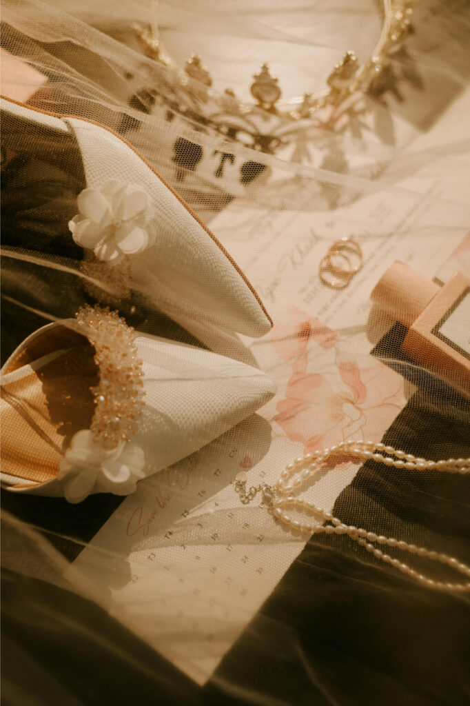 Soft, romantic wedding detail flat lay with rings, invitation, and veil, styled for a stress free wedding aesthetic