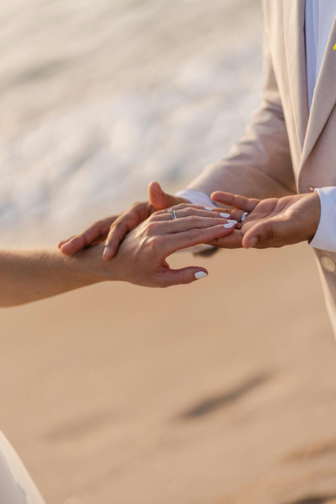 Close up of couple exchanging rings on beach, intimate moment