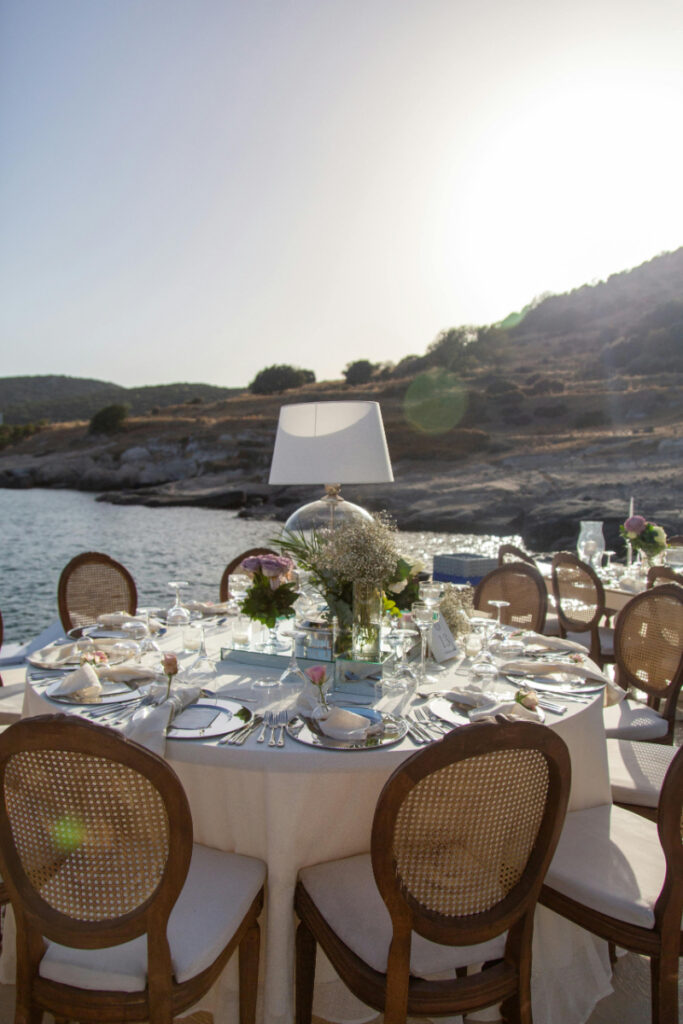 Outdoor wedding reception table by the water, elegant place setting with florals and sunset view